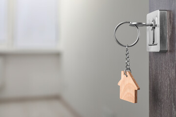 Wall Mural - Mortgage and real estate. Open door with key and house shaped keychain against blurred background, space for text