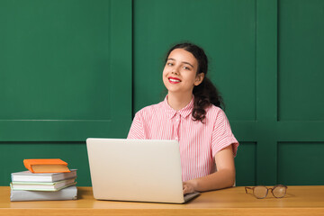 Wall Mural - Female student with laptop doing homework at table near green wall