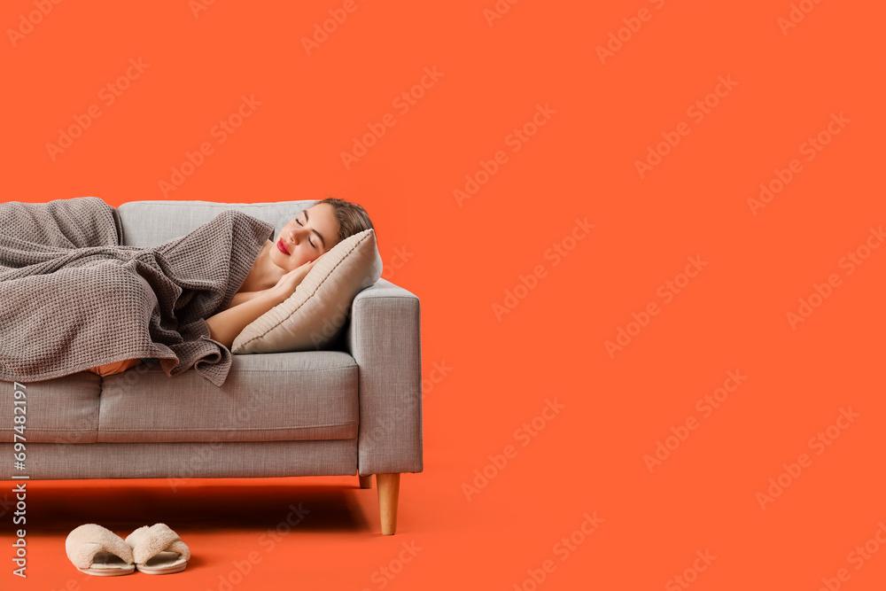 Young woman with plaid sleeping on grey sofa against orange background