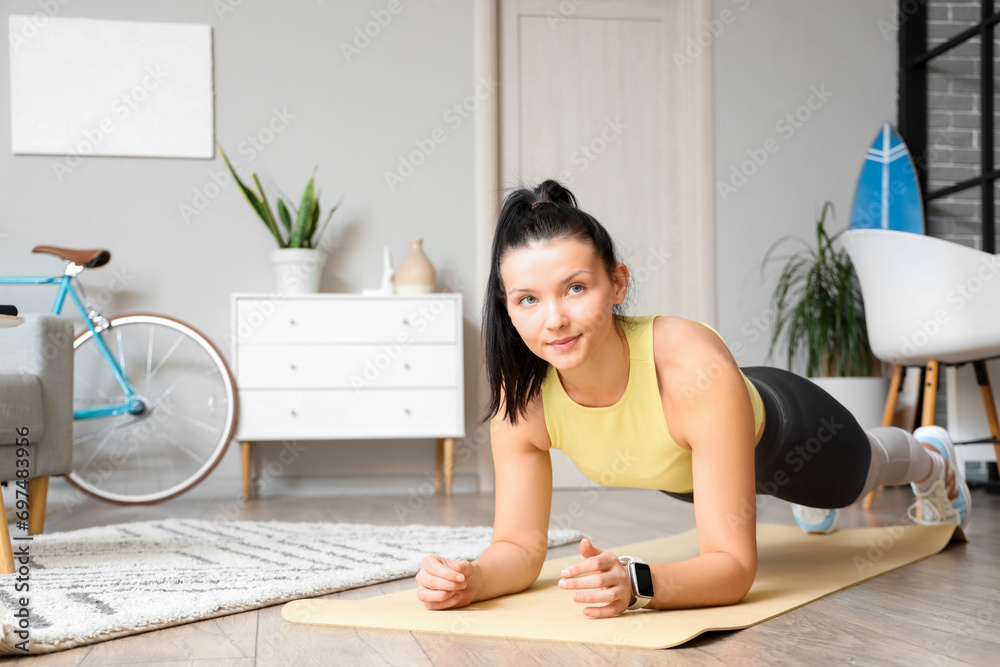 Sporty young woman doing plank on mat at home