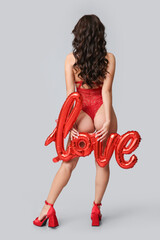 Wall Mural - Beautiful young Asian woman with balloon in shape of word LOVE wearing sexy underwear on grey background, back view