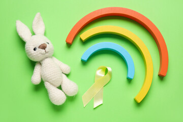 Poster - Golden ribbon with toys on green background. Childhood cancer awareness concept