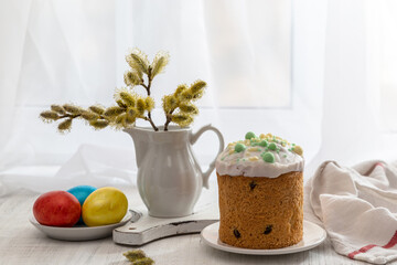 Wall Mural - Easter still life with colored eggs, Easter cake and willow in a milk jug on the windowsill on a sunny day.