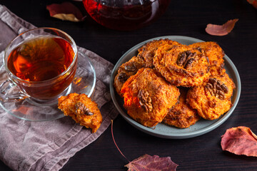 Wall Mural - Carrot cookies with walnuts and tea in a cup against a dark background.