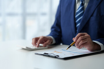 Wall Mural - Businessman uses pen to point at chart Graph and use ideas to analyze financial reporting situations. Calculate your investments with the income, tax and accounting calculators at your desk.