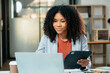 © laddawan - Young woman typing on tablet and laptop while sitting at the working in office