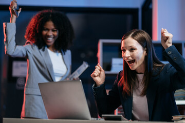 Successful business team, excited young people Keeping up arms and showing positive emotions, happy working in modern office on computer.