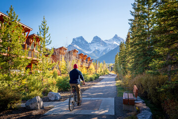 people riding a bicycle on trail in residential area. town of canmore street view in fall season. al