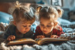 Two children lie on their tummies and read the same book together