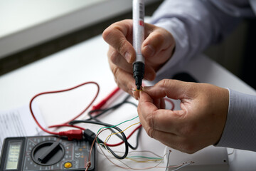 Male hands with a felt-tip pen marking an electric wire. Nearby is an electrical measuring device.