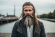 handsome bearded hipster man with long beard and mustache on serious face in leather jacket outdoor on blurred background