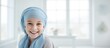 Cheerful girl with kidney cancer wearing blue headscarf photographed indoors after chemotherapy.