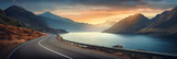 Fototapeta Natura - Coastal road winding through a scenic landscape with mountains, ocean, and clear skies at dawn.