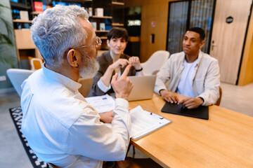 Canvas Print - Group of mixed age colleagues discussing business issues during meeting in conference room