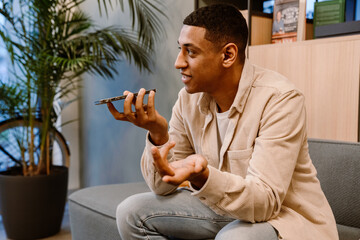 Positive man sending voice message using smartphone while sitting in coworking