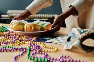 Young unrecognizable African American woman putting plate with appetizing homemade pastry on table with beads and mask