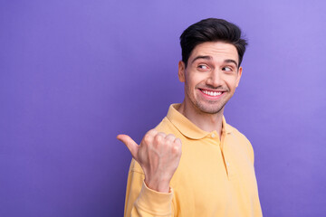 Sticker - Photo of good mood dreamy guy wear yellow polo looking showing thumb back empty space isolated violet color background