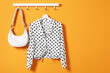 Hanger with polka dot shirt and bag on orange wall, space for text