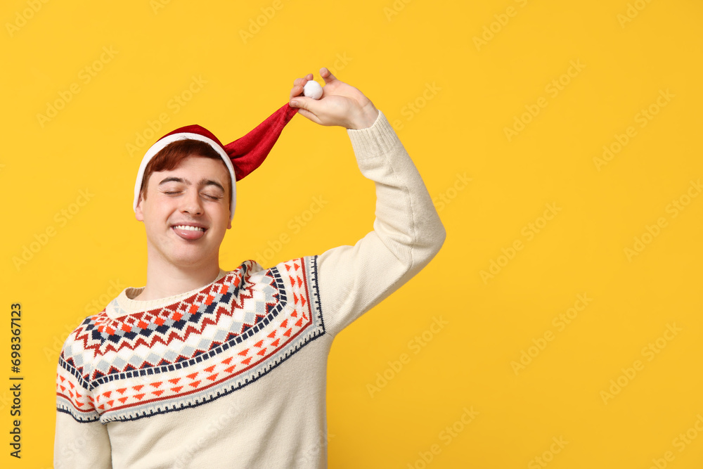 Handsome young man in warm sweater and Santa hat on yellow background