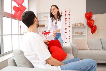 Canvas Print - Happy young woman greeting her husband with gift at home on Valentine's Day