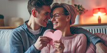 Portrait Of Couple Holding Paper Heart And Happy Smiling Couple In Love Celebrating Their Relationship Anniversary Or Valentine's Day At Home. Couple Love Moments Happiness And Valentine's Day Concept