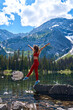 Beautiful slender woman in sports suit poses on big stone in calm clear lake with reflection of high mountains with snow in summer. Young girl resting by the water while hiking in Kananaskis Alberta.