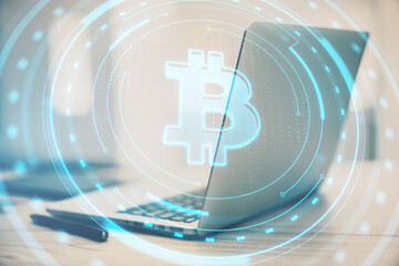 Wall Mural - Close up of laptop on desk with creative round hologram with bitcoin on blurry background. Money, online banking and finance concept. Double exposure.