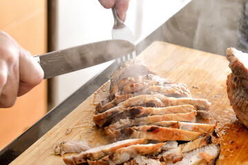 Roasted pork slices on bamboo chopping board. Christmas meal cooking preparation. Steam smoke on food.