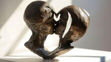  A Close Up Of A Sculpture Of A Man And A Woman In The Shape Of A Heart With A Shadow Of A Building On The Side Of A White Wall.