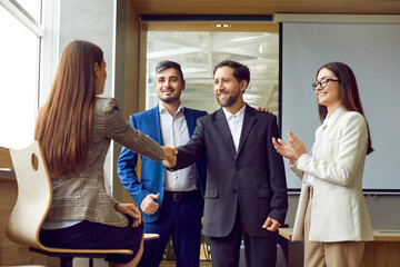 Wall Mural - Business people greet each other as they meet in the office. Happy man and woman shake hands as they come to a work meeting with their colleagues. Professional teamwork and partnership concept