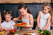 © dvulikaia - Little girl is preparing vegetarian salad and adding chopped tomatoes to bowl together with her younger sisters.