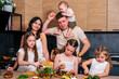 © dvulikaia - Large family - mom, dad, three daughters and baby son together prepare salad for lunch in modern kitchen. Big family together concept.