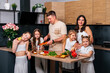 © dvulikaia - Large family - mom, dad and four daughters together prepare salad for lunch in modern kitchen. Big family together concept.