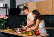 © dvulikaia - Young man cooking salad at the kitchen and his happy wife hugging him.