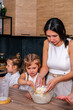 © dvulikaia - Young mother cooks sweet cottage cheese pie with her daughters. Mom teaches her daughters to cook.