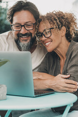 Wall Mural - One couple middle age enjoy and have fun together using laptop sitting outdoor at the table in the garden at home. Man and woman in love and friendship doing video web call together smiling. Happiness