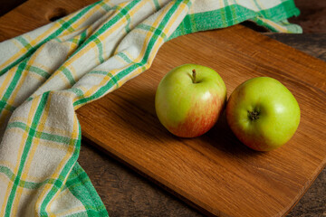 Cutting board with two green apples on wooden background with green kitchen towel..