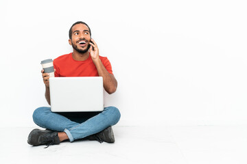 Sticker - Young Ecuadorian man with a laptop sitting on the floor isolated on white background holding coffee to take away and a mobile