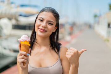 Canvas Print - Young pretty woman with a cornet ice cream at outdoors pointing to the side to present a product