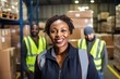 © Rudsaphon - Portrait of smiling african american female warehouse worker standing in warehouse with colleagues in background