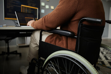 Close up of unrecognizable man with disability using wheelchair while working at desk in office, copy space