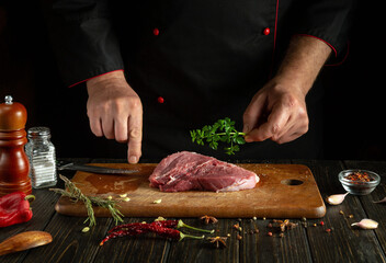 Wall Mural - In the hand of the cook is fresh parsley for steak meat. Cooking grilled lamb on the kitchen table with spices and garlic.