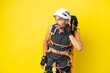 Young caucasian rock climber man isolated on yellow background listening to something by putting hand on the ear
