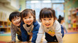 日本の幼稚園児・保育園児3人が長袖の私服で横に並んでハイハイでカメラに笑いながら向かってきている写真、背景教室、保育室のボケ