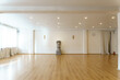 A spacious empty hall with columns and large windows. A gym with wooden floors for yoga and fitness classes. Interior design of the fitness center. A large room without furniture.