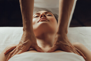 Hands of female chiropractor massaging shoulders of young woman lying on massage table. Concept of physical therapy treatment ,neck pressure point