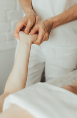 Wall Mural - Hands of female chiropractor massaging palms of young woman lying on massage table on white background. Concept of physical therapy treatment, neck pressure point