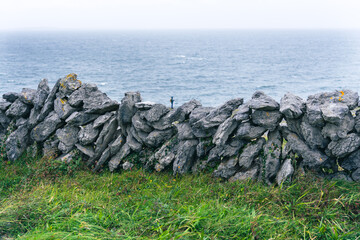 Wall Mural - Beautiful view of the stone wall in the center with the sea in the background with a person completely alone in the distance giving a feeling of immensity and loneliness