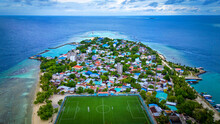 Drone Aerial View Of Maldives Island In The Indian Ocean With Soccer Field In View And Blue Waters