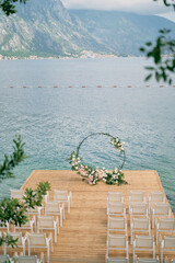 Poster - Rows of white chairs stand on the pier in front of a round wedding arch